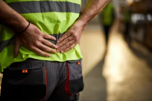 Close up of manual worker holding his back in pain at distribution warehouse.